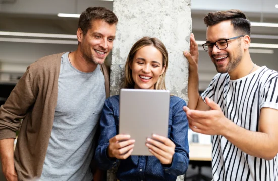 Trois collègues souriants regardent une tablette ensemble dans un bureau, illustrant la collaboration et les usages numériques en entreprise.